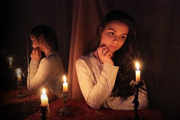 Noia asseguda al mirall amb espelmes